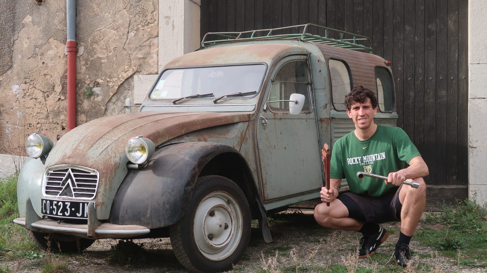 Aurélien, outils en main, devant sa 2CV fourgonnette